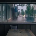 Rain-speckled café window with a quiet table and chairs outside