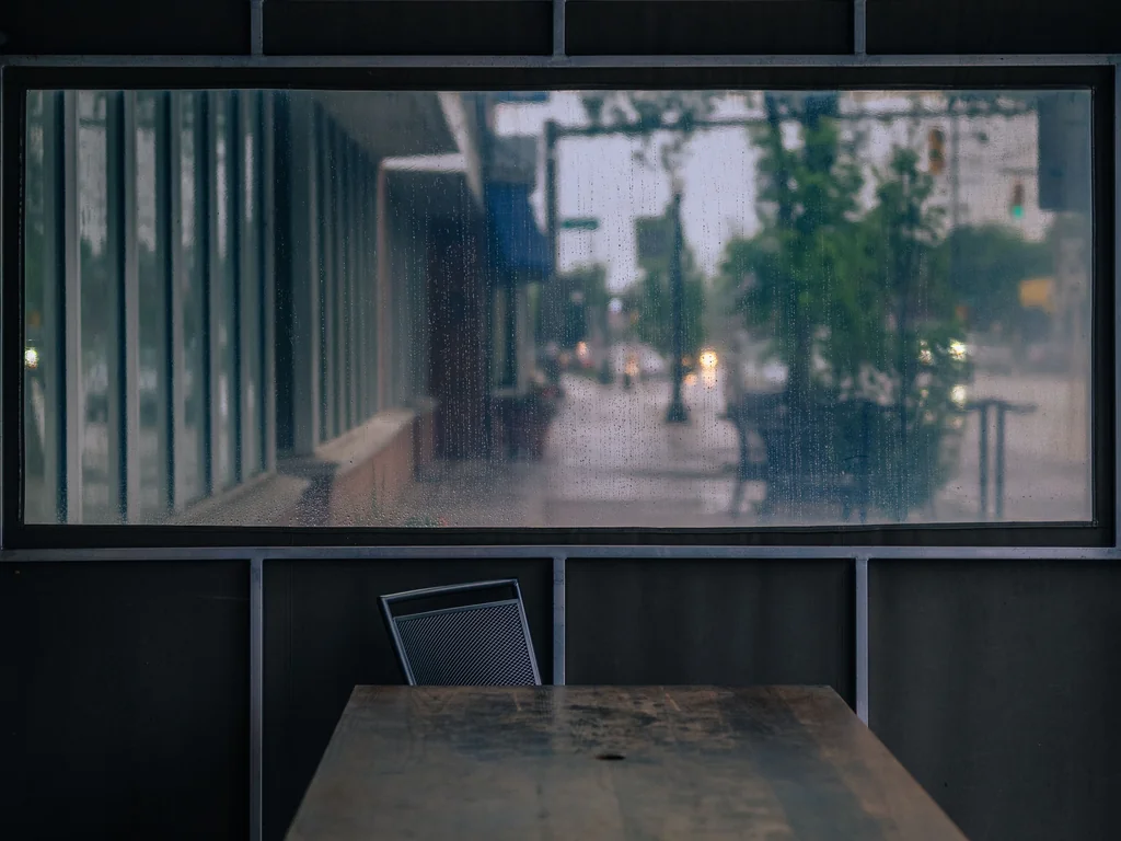 Rain-speckled café window with a quiet table and chairs outside