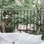 White bedding beside an open balcony overlooking green trees