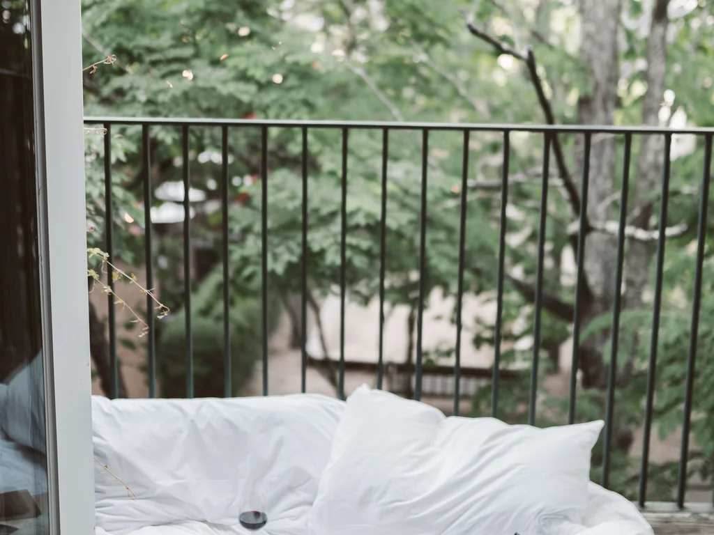 White bedding beside an open balcony overlooking green trees